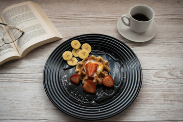 Delicious waffle with fruits on a table with a coffee and a book