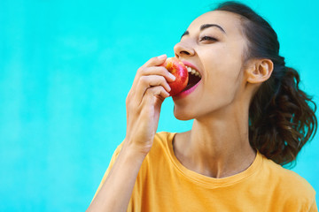 Portrait of healthy young woman biting juicy ripe apple with delighte, healthy snack fresh ripe, posing on a colorful bright cyan background.