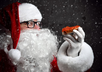 Smiling Santa Claus is holding red salmon caviar sandwich, looking glancing at us going to eat...