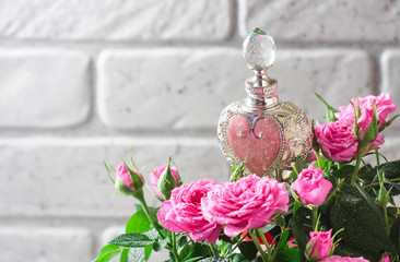 Natural pure rose oil or scented water in bottles for spa, skin care or aromatherapy. Glass bottle on a wooden table, small pink roses with leaves. Organic cosmetics concept.