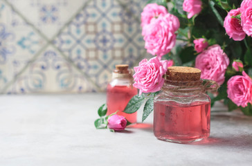 Natural pure rose oil or scented water in bottles for spa, skin care or aromatherapy. Glass bottle on a wooden table, small pink roses with leaves. Organic cosmetics concept.