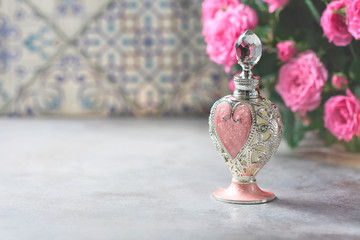 Natural pure rose oil or scented water in bottles for spa, skin care or aromatherapy. Glass bottle on a wooden table, small pink roses with leaves. Organic cosmetics concept.