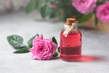 Natural pure rose oil or scented water in bottles for spa, skin care or aromatherapy. Glass bottle on a wooden table, small pink roses with leaves. Organic cosmetics concept.