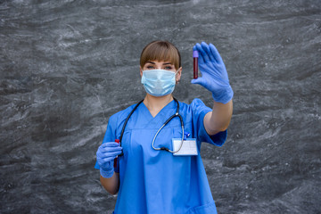 Young nurse with medical face mask is pointing at blood probe in laboratory. Medical concept.