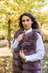 Woman wearing fashionable fur coat walking in autumn park.