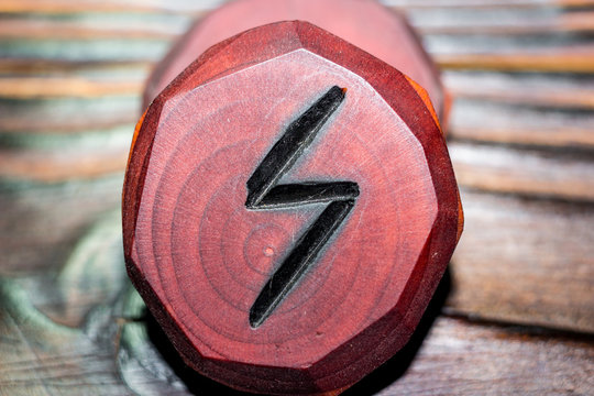 Rune Sowilo (Sigel, Sol) red color carved from wood on a wooden background - Elder Futhark