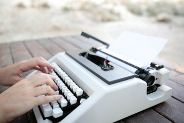 Manos de persona tecleando en máquina de escribir vintage en mesa de madera vista lateral