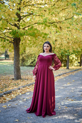 Young princess  in a beautiful red dress in park. The background is bright, golden autumn nature.