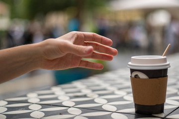 A hand reaches for dark vending coffee in disposable kraft paper cup and plastic lid on table at street cafe.