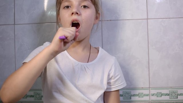 eight-year-old girl in white t-shirt brushes teeth in bathroom. Health care, hygiene and childhood concept. Caries prevention, morning or evening routine