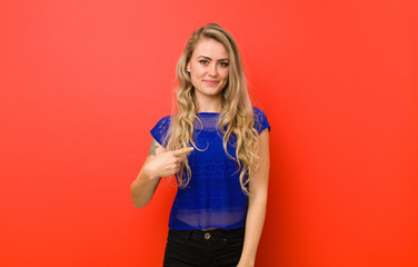 young blonde woman looking proud, confident and happy, smiling and pointing to self or making...