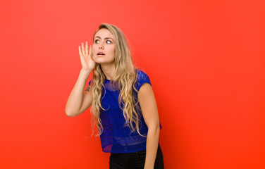 young blonde woman looking serious and curious, listening, trying to hear a secret conversation or...