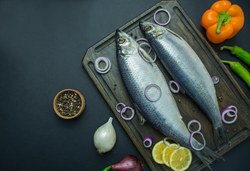 Salted herring with onions and herbs on a cutting board. Dark background. Space for text.