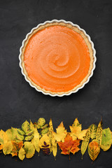 Bright orange pumpkin pie and dry leaves looking like sunset over autumn forest on black background. Healthy natural sweets concept