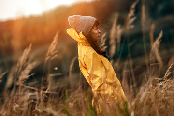 Young female with yellow raincoat in tall grass during sunset light - Windy outdoors weather