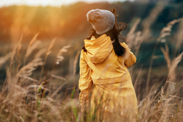 Young female with yellow raincoat in tall grass during sunset light - Windy outdoors weather