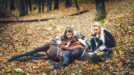 Viking warrior women hiding and stalking on raid battle with horse laying on forest 