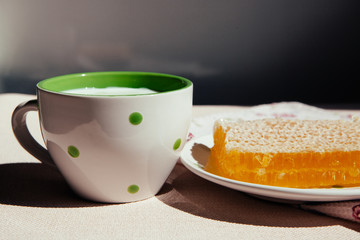Cup of milk with honey on table with sunshine on background, healthy sweet food
