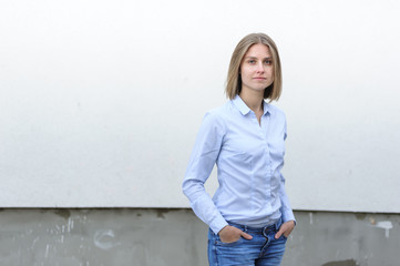 Blonde bussiness woman dressed casual with a perfect smile, standing near a white wall