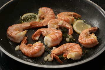 roasted tiger prawn shrimps in a black pan with garlic, lemon and herbs, close up shot