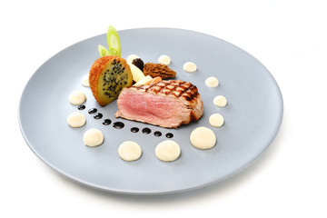 roasted veal, morels, vegetables and a fried potato stuffed with onion seeds on a blue plate,...