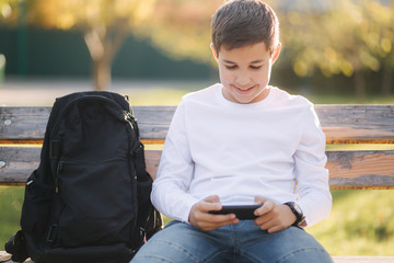 Teenage boy play online games on his smartphone in the park after lessons in school