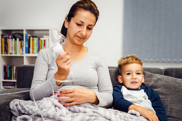 Woman mother with her small son boy child make him using vapor steam inhaler nebulizer mask...