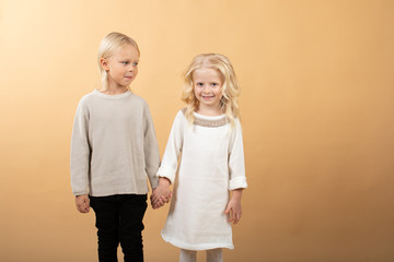 A little girl in a white knitted dress and a black hat and a boy in a sweater. Children holding hands