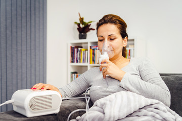 Woman lying covered with blanket using vapor steam inhaler nebulizer mask inhalation at home on the bed medicament treatment asthma pneumonia bronchitis coughing sick - obrazy, fototapety, plakaty