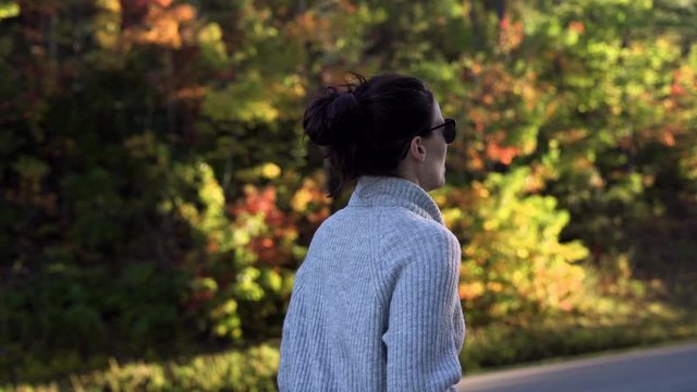 Slow motion young attractive woman outside in nature during golden hour with sunglasses on during fall season with changing leaves on tress walking and exploring
