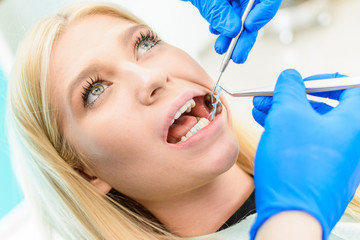 Image of pretty young woman sitting in dental chair while professional doctor fixing her teeth