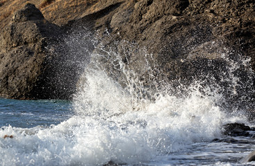 The wave breaks into small splashes on a rocky shore