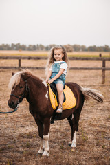 Adorable little girl riding a pony at summer