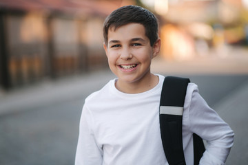 Close up portrait of happy smiled teenage boy in white sweatshirt with backpack outside