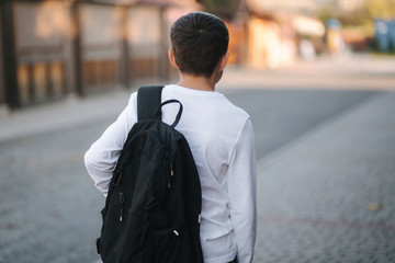 Back view of boy in white shirt with black backpack go home after the lesson