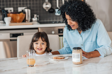 Smiling little girl eating breakfast with her mother at home - Powered by Adobe