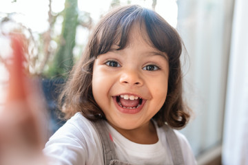 Smiling little girl taking a selfie while playing at home