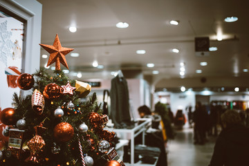 Vintage film effect over elegant Christmas tree decorated with red glass bulbes inside large supermarkt fashion mall people customers shopping in background