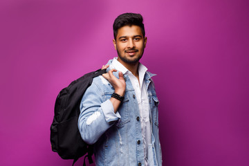 Portrait of handsome Indian guy, with bag on back, study time, standing on violet background, copy...