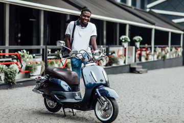 Fototapeta na wymiar Handsome man riding a scooter on city roads. Summer potrait of male wearing a white shirt sitting near retro motorbike.