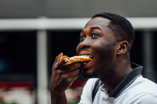 Young Man Eats A Piece Of Appetizing Pizza. Hungry Guy Holds A Piece Of Pizza In His Hands, Looks At Him And Is Going To Eat It.