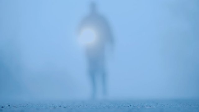 Blurred silhouette of a man in the fog with a bloody ax with an ax and a flashlight