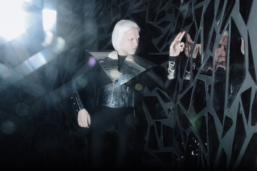 Fototapeta na wymiar young blonde caucasian man standing in alien cosmos halloween costume and looking near the many mirrors and reflecting on black background