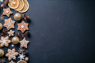 Obraz na płótnie Canvas Winter holiday vibes. Border made of festive decorations, dried oranges and gingerbread on black background. Seasonal background, Christmas, New Year composition. Flat lay, copy space