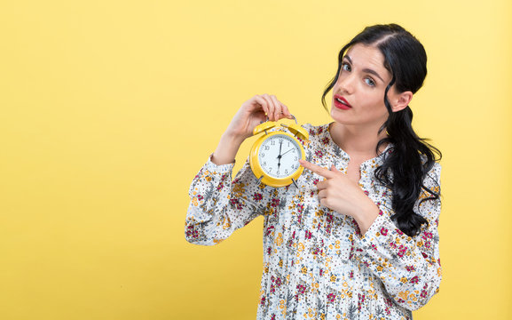 Yong woman holding a clock showing 6AM on a yellow background