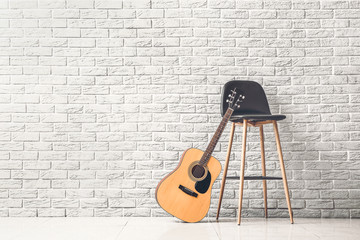 Modern acoustic guitar and chair near white brick wall