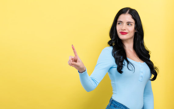 Young woman pointing at something on a yellow background