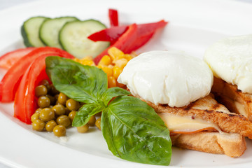 Ñrispy toast with ham and cheese, poached eggs, fresh vegetables and sauce.