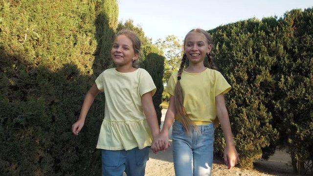 Little girls running in a hedge maze, two sisters kids hold hands and run in big green labyrinth in city park