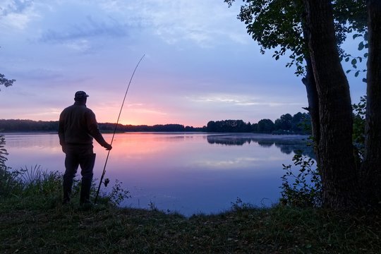 Silhouette fisherman standing on the shore of the lake during dawn